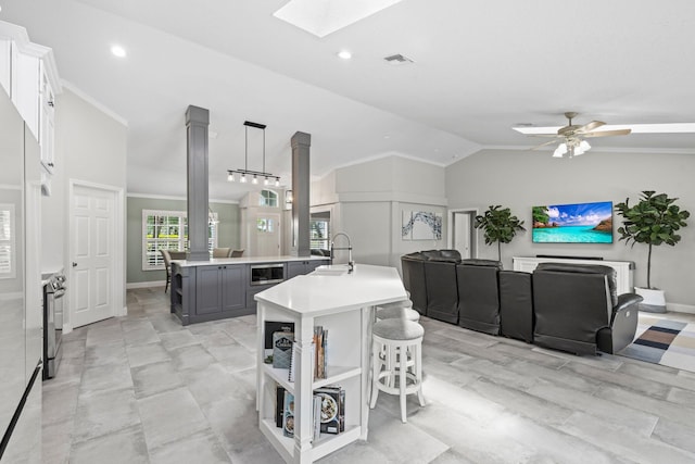 kitchen featuring gray cabinetry, sink, lofted ceiling with skylight, decorative light fixtures, and a kitchen island with sink