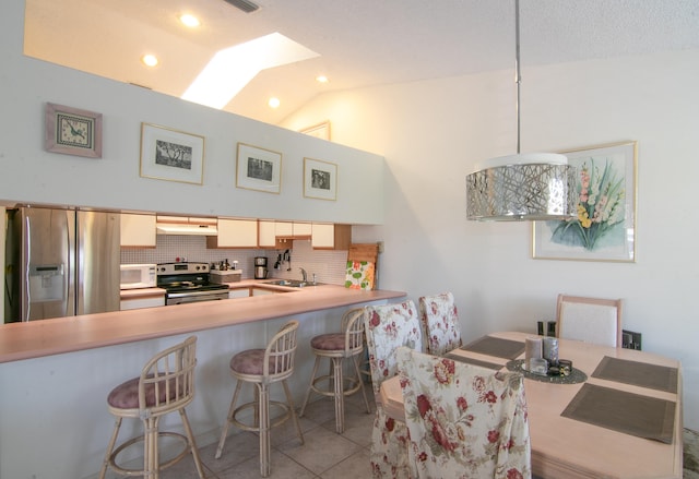 kitchen featuring kitchen peninsula, appliances with stainless steel finishes, backsplash, lofted ceiling with skylight, and a breakfast bar area