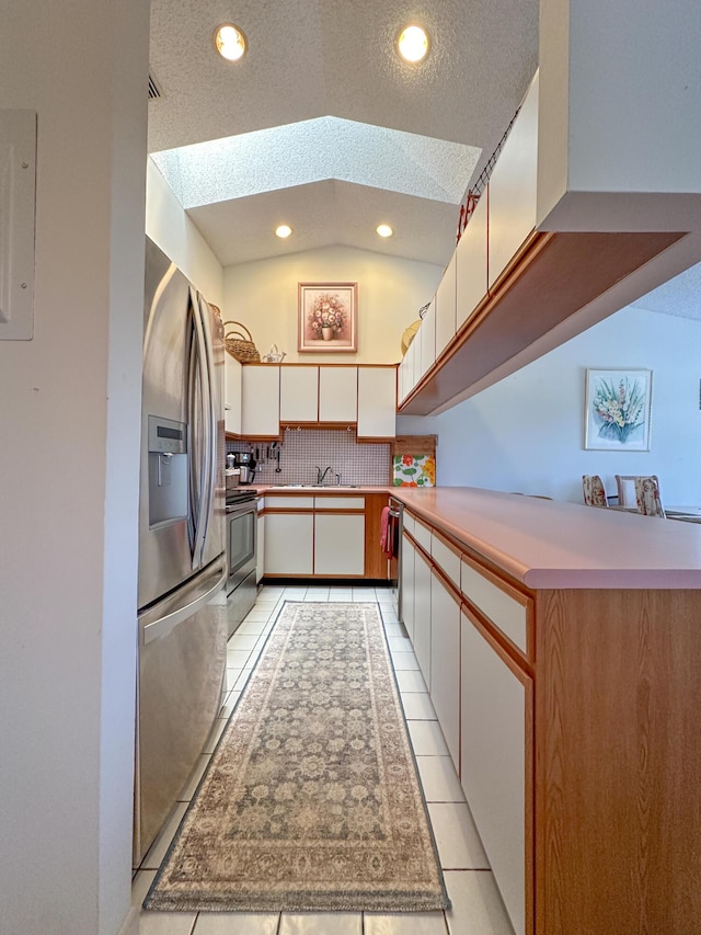 kitchen featuring white cabinets, range with electric cooktop, vaulted ceiling with skylight, a textured ceiling, and stainless steel fridge with ice dispenser