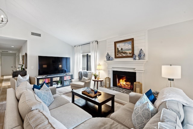 living room featuring hardwood / wood-style flooring, a notable chandelier, a large fireplace, and lofted ceiling