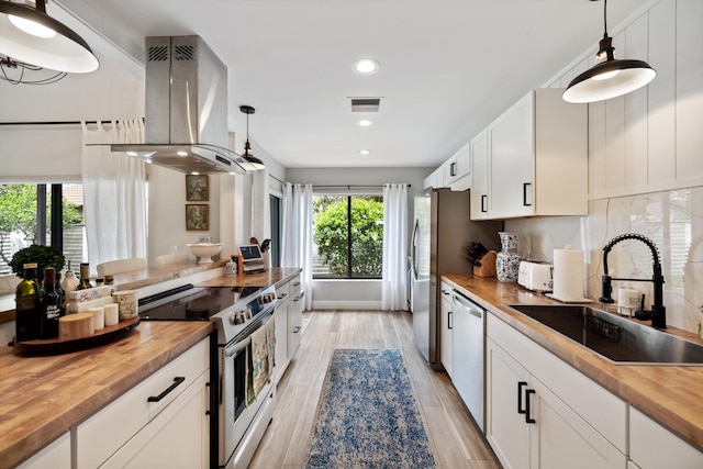 kitchen with wooden counters, decorative light fixtures, stainless steel appliances, and island range hood