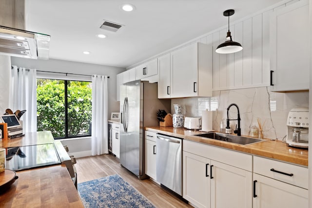 kitchen featuring stainless steel appliances, sink, pendant lighting, white cabinets, and light hardwood / wood-style floors