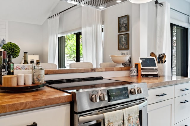 kitchen featuring white cabinets, vaulted ceiling, stainless steel range, and wooden counters