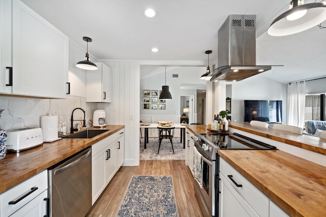 kitchen with wood counters, stainless steel appliances, hanging light fixtures, and island range hood