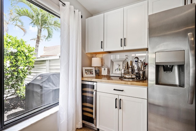 bar featuring white cabinets, stainless steel refrigerator with ice dispenser, beverage cooler, and wooden counters