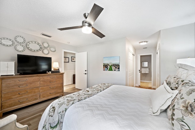 bedroom with ensuite bath, a textured ceiling, ceiling fan, hardwood / wood-style floors, and a closet