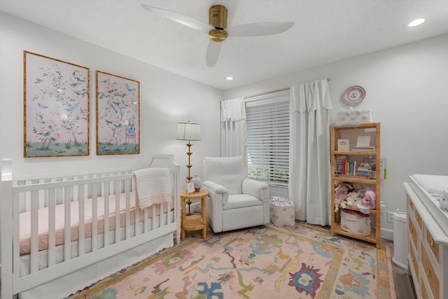 bedroom featuring a textured ceiling, a nursery area, and ceiling fan