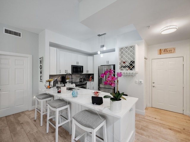 kitchen with kitchen peninsula, stainless steel refrigerator with ice dispenser, a kitchen breakfast bar, white cabinets, and hanging light fixtures