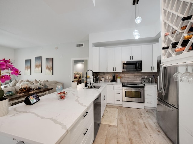 kitchen featuring appliances with stainless steel finishes, light stone counters, sink, decorative light fixtures, and white cabinets