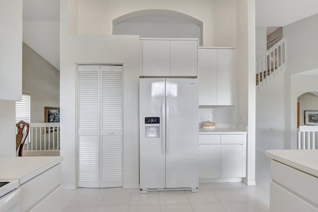 kitchen featuring white cabinetry, light tile patterned floors, a towering ceiling, and white refrigerator with ice dispenser