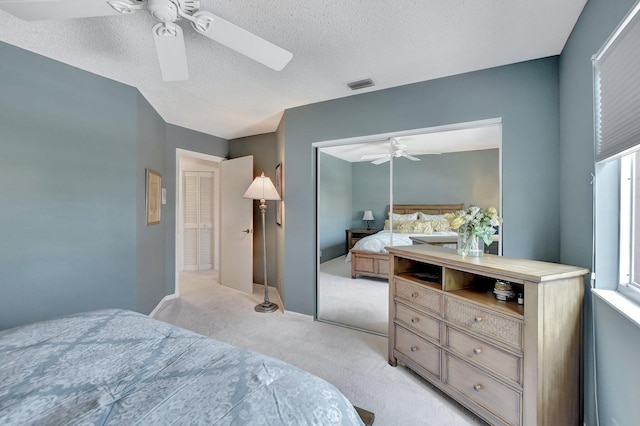 bedroom with ceiling fan, a textured ceiling, light carpet, and a closet