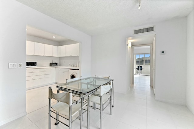 dining space featuring light tile patterned flooring, a textured ceiling, and washer / dryer