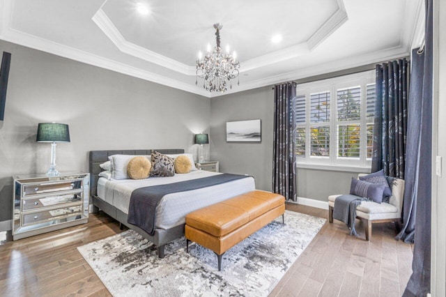 bedroom with hardwood / wood-style floors, a tray ceiling, an inviting chandelier, and crown molding