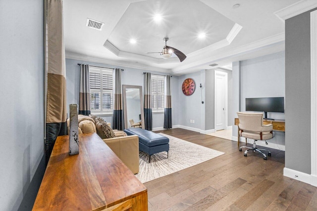 living room featuring hardwood / wood-style floors, a raised ceiling, ceiling fan, and ornamental molding