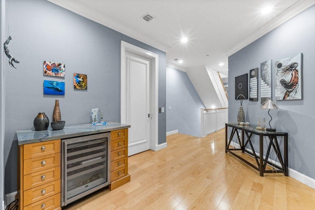 bar with light stone countertops, light wood-type flooring, ornamental molding, and wine cooler