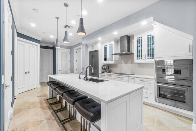 kitchen with a center island with sink, wall chimney exhaust hood, white cabinetry, and sink