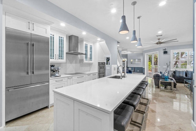 kitchen with wall chimney exhaust hood, stainless steel appliances, a spacious island, sink, and white cabinetry