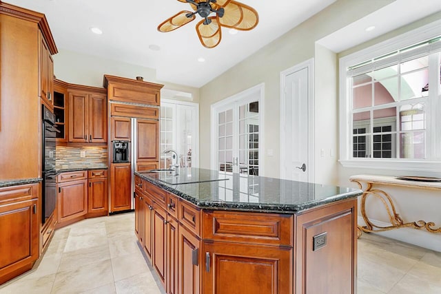 kitchen featuring french doors, dark stone counters, ceiling fan, a center island with sink, and paneled built in fridge