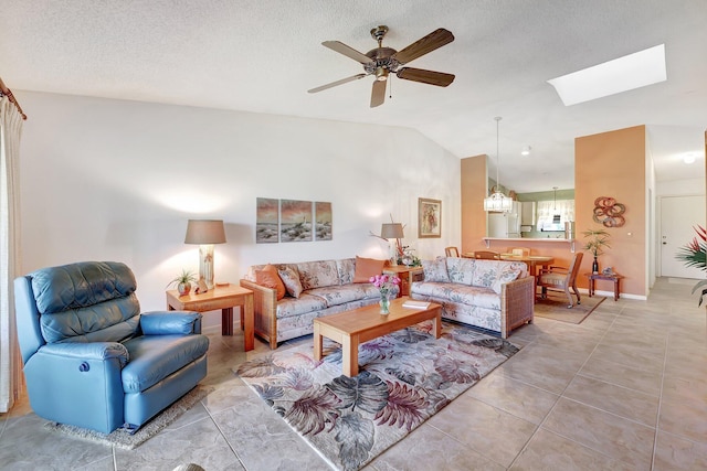 tiled living room with a textured ceiling, lofted ceiling with skylight, and ceiling fan