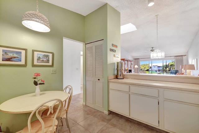 kitchen with pendant lighting, lofted ceiling, white cabinets, light tile patterned floors, and a textured ceiling