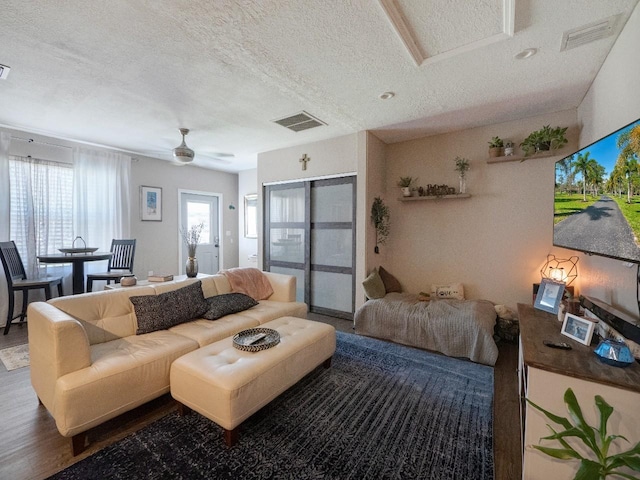 living room with a textured ceiling, ceiling fan, and dark wood-type flooring