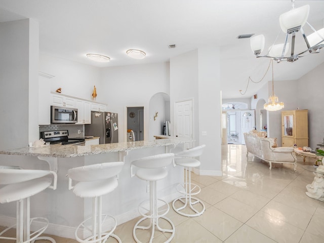 kitchen featuring a kitchen bar, appliances with stainless steel finishes, kitchen peninsula, light tile patterned floors, and white cabinetry