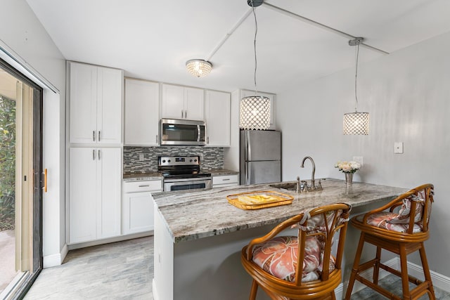 kitchen with a kitchen bar, stainless steel appliances, sink, pendant lighting, and white cabinets