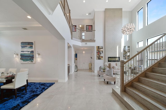 foyer entrance featuring a towering ceiling, a fireplace, and ornamental molding