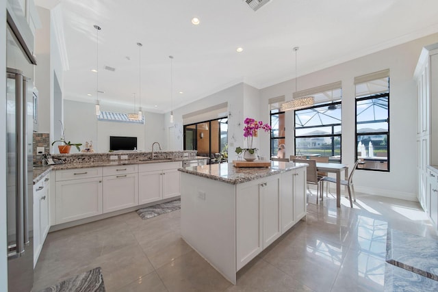 kitchen featuring light stone countertops, white cabinetry, sink, a center island, and pendant lighting