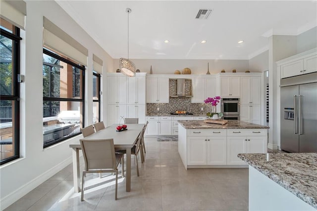 kitchen with pendant lighting, wall chimney exhaust hood, light stone countertops, and appliances with stainless steel finishes