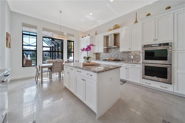 kitchen featuring white cabinetry, light stone countertops, wall chimney range hood, decorative light fixtures, and appliances with stainless steel finishes