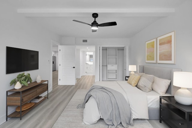 bedroom with beamed ceiling, ceiling fan, a closet, and light wood-type flooring