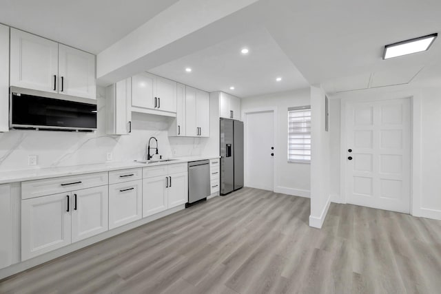 kitchen with white cabinets, appliances with stainless steel finishes, light countertops, light wood-type flooring, and a sink