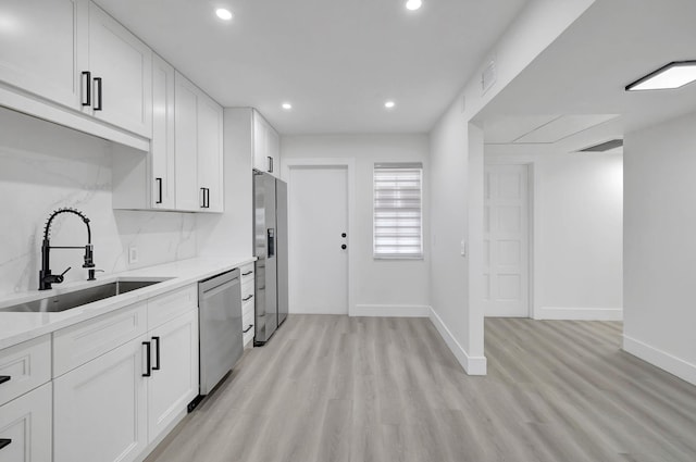 kitchen with stainless steel appliances, a sink, white cabinetry, light countertops, and backsplash