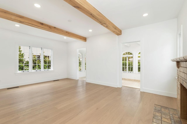 unfurnished living room featuring beamed ceiling, plenty of natural light, light hardwood / wood-style floors, and a brick fireplace