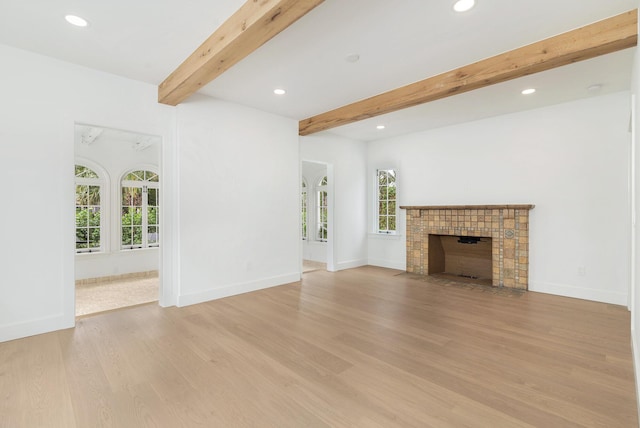 unfurnished living room featuring beamed ceiling, light hardwood / wood-style floors, and plenty of natural light