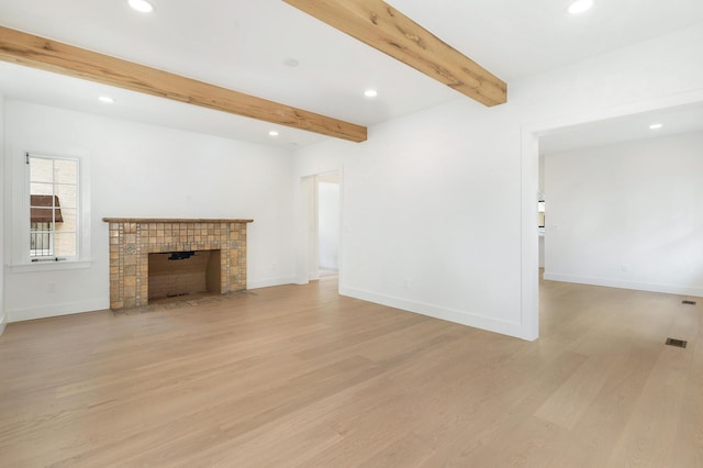 unfurnished living room with a tile fireplace, light hardwood / wood-style floors, and beamed ceiling