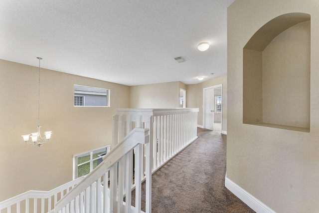 hallway with an inviting chandelier and dark colored carpet