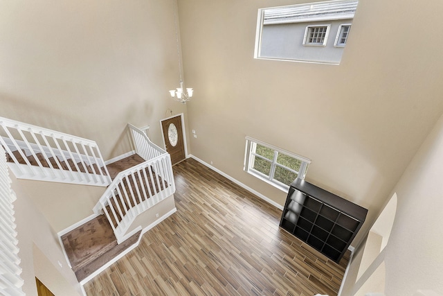 stairs with a towering ceiling, hardwood / wood-style flooring, and a notable chandelier