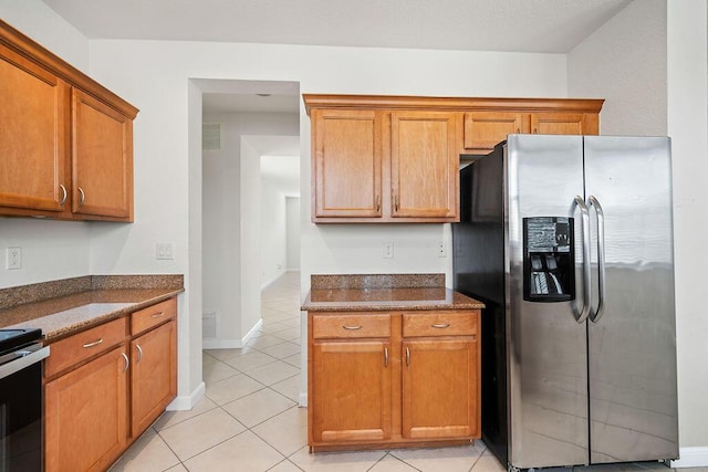 kitchen featuring stove, light tile patterned flooring, dark stone counters, and stainless steel refrigerator with ice dispenser