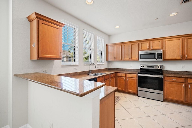 kitchen with kitchen peninsula, appliances with stainless steel finishes, dark stone counters, sink, and light tile patterned flooring