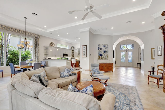 tiled living room with ceiling fan with notable chandelier, a raised ceiling, and crown molding