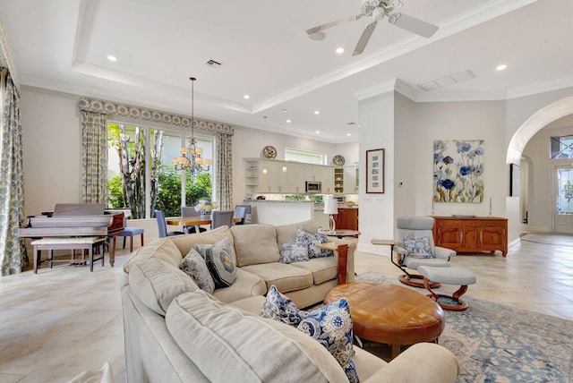 tiled living room featuring a raised ceiling, crown molding, and ceiling fan with notable chandelier