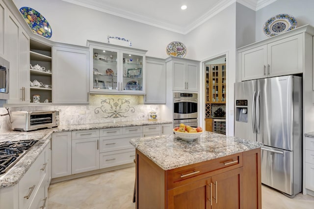 kitchen featuring backsplash, white cabinets, light stone countertops, appliances with stainless steel finishes, and a kitchen island