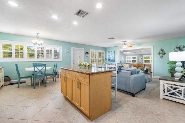 kitchen with a kitchen island, dark stone countertops, pendant lighting, light tile patterned flooring, and ceiling fan with notable chandelier