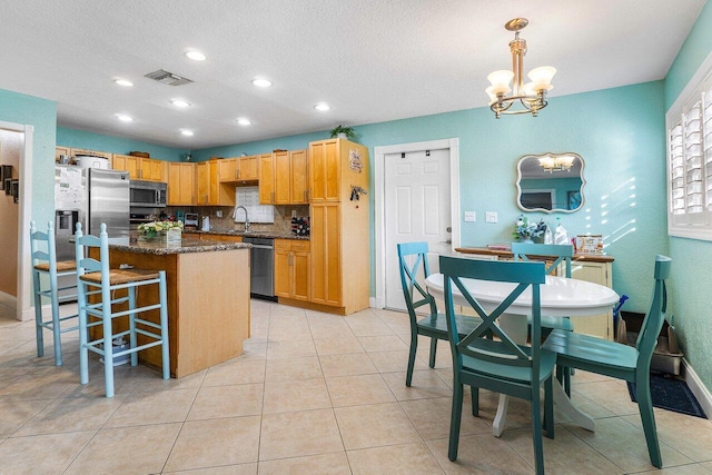 kitchen featuring pendant lighting, a center island, backsplash, appliances with stainless steel finishes, and a chandelier