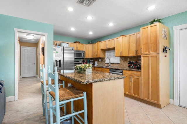 kitchen featuring stainless steel appliances, a kitchen breakfast bar, tasteful backsplash, dark stone counters, and a kitchen island