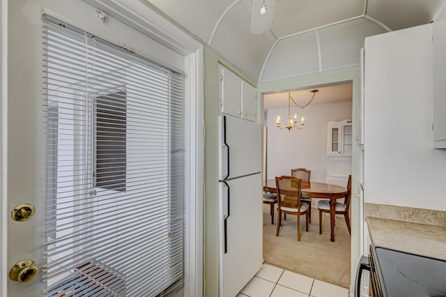 kitchen featuring white cabinetry, white fridge, vaulted ceiling, decorative light fixtures, and light tile patterned flooring