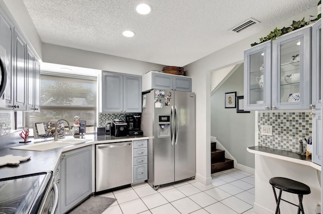 kitchen featuring gray cabinetry, decorative backsplash, light tile patterned floors, a textured ceiling, and stainless steel appliances