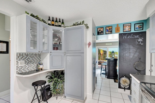 kitchen featuring a textured ceiling, white cabinets, light tile patterned floors, and backsplash